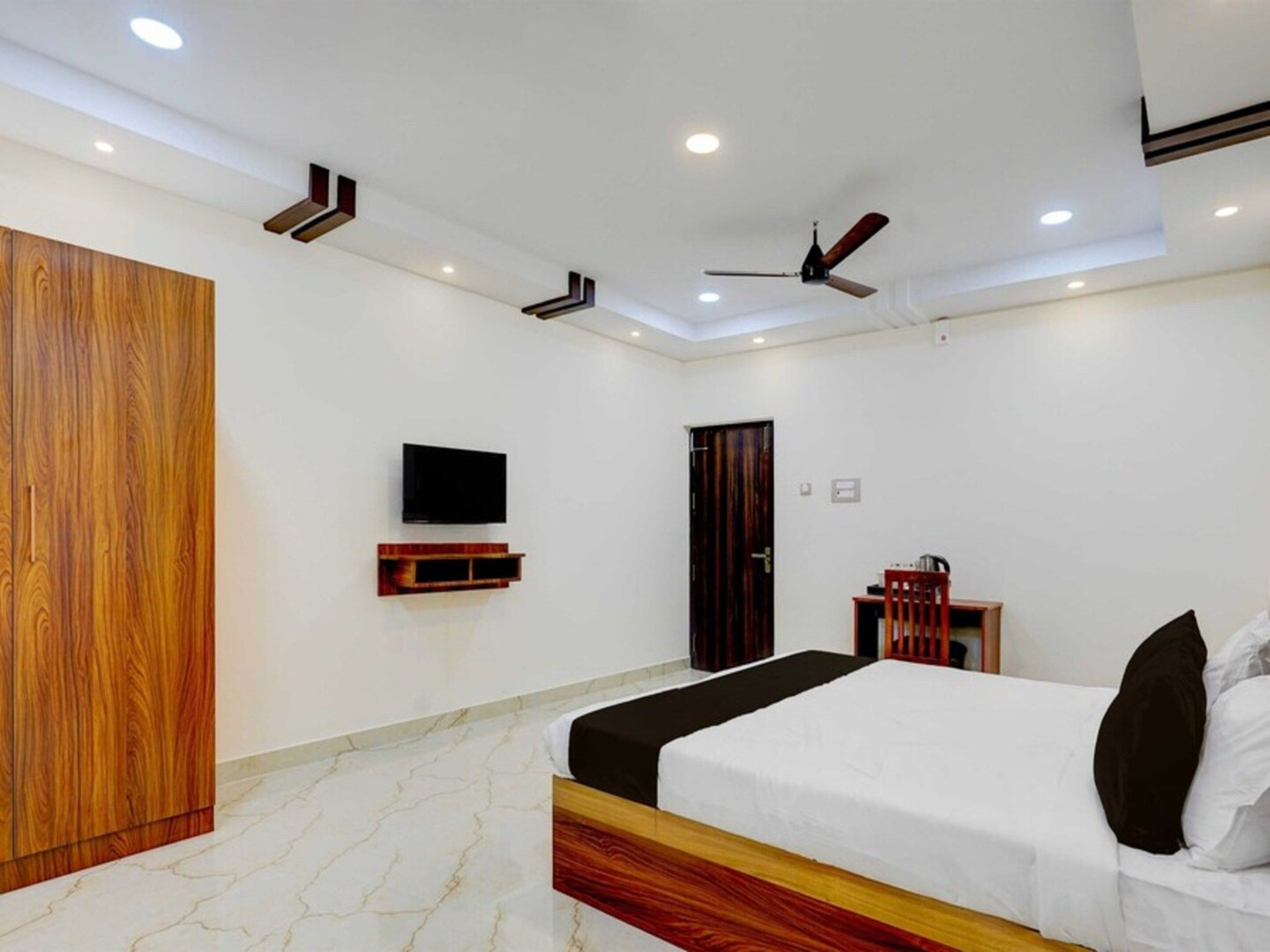 A bedroom with a bed, a TV, a wardrobe, a ceiling fan, and a door.