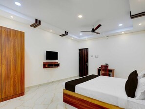 A bedroom with a bed, a TV, a wardrobe, a ceiling fan, and a door. - Deluxe Room Saibala Lodge (Vellore)