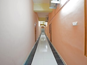 A corridor with doors on both sides, a tiled floor, and a ceiling with an air conditioning unit. - Deluxe Room Saibala Lodge (Vellore)