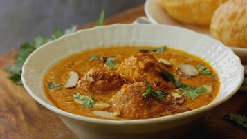 A bowl of curry with meat and garnishes, accompanied by bread on a table.