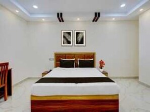 A hotel room with a large bed, a wooden headboard, a nightstand, and two framed pictures on the wall.