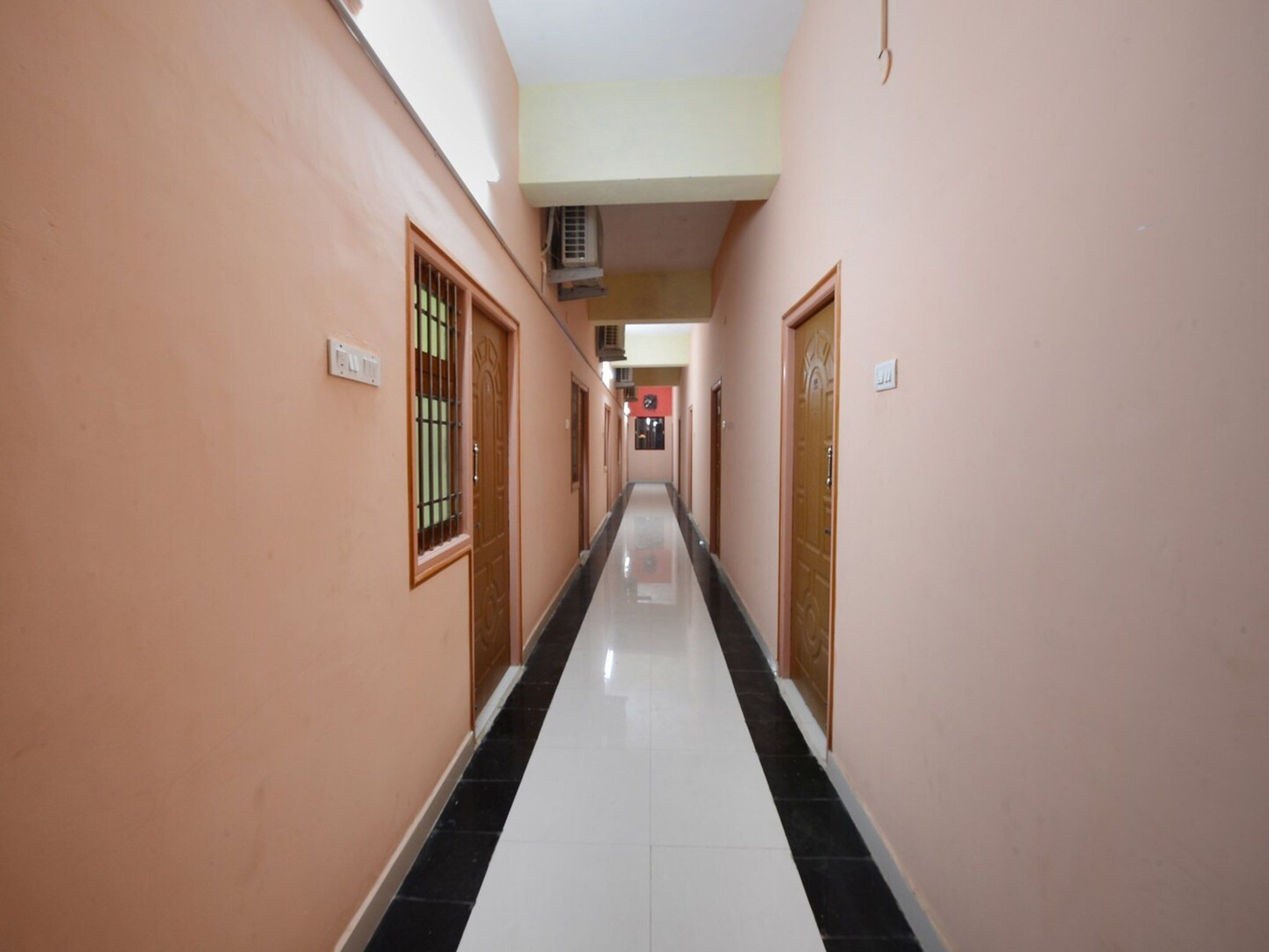 Un corridoio con porte su entrambi i lati, un pavimento piastrellato e un condizionatore d'aria a soffitto.
