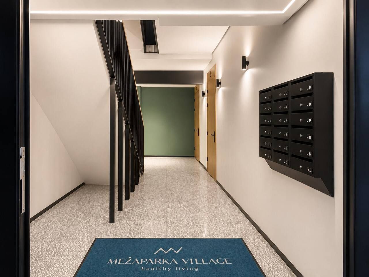 Un couloir avec un tapis bleu, un escalier et une boîte aux lettres fixée au mur.
