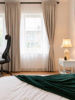 Quarto de hotel com cama, cadeira, luminária e janela com cortinas.