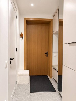 Um corredor com porta de madeira, um banco branco e um tapete preto.