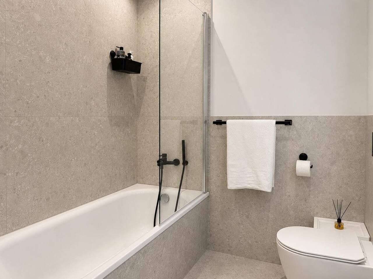 A modern bathroom with a glass-enclosed shower, a white bathtub, and a toilet.