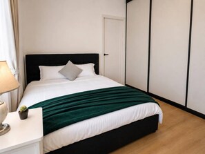Ein ordentlich bezogenes Bett mit dunklem Kopfteil, weißer Bettwäsche und einer grünen Decke.