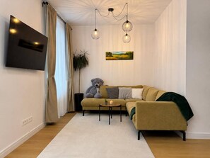 Ein modernes Wohnzimmer mit einer Couch, einem Couchtisch, einem großen Teddybären, einem Gemälde und einem an der Wand befestigten Fernseher.