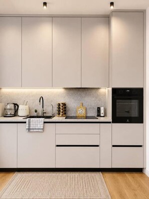 A modern kitchen with built-in appliances, a countertop with a kettle, toaster, and a coffee maker, and a wooden cutting board.