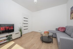 A modern living room with a flat-screen TV, a grey sofa, a coffee table, and a bookshelf. - Lumina 2-room Apart near Skaryszewski (Warszawa)