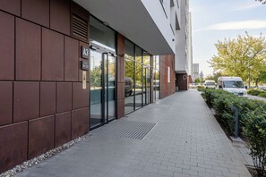 Un edificio moderno con entrada de vidrio, un sendero pavimentado y un estacionamiento con vehículos.