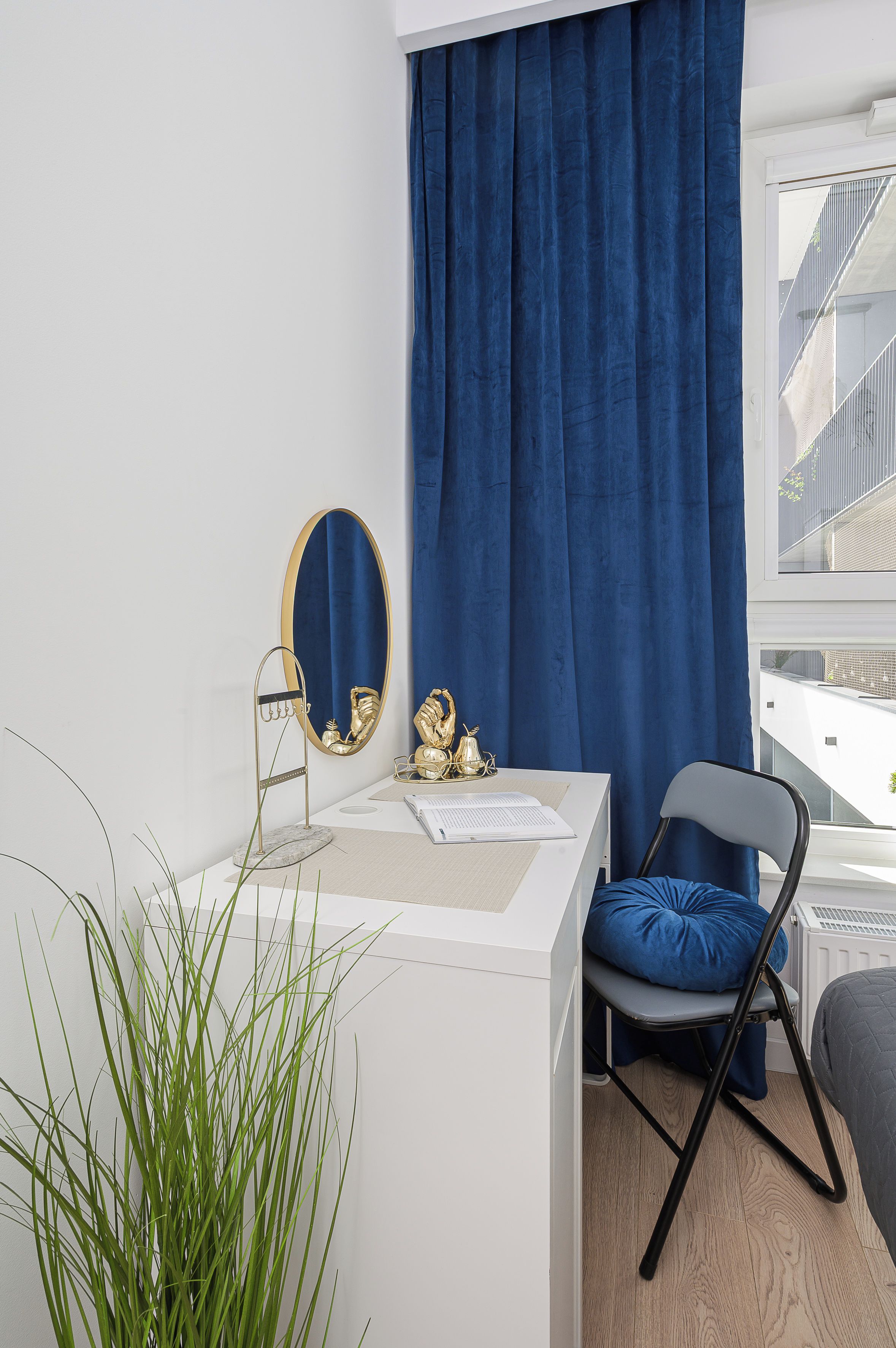 A modern room with a white desk, a blue chair, a large mirror, and a view of the outside.
