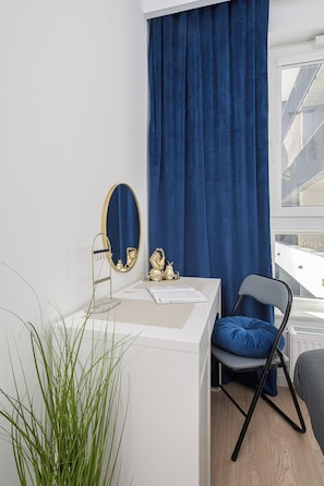 Habitación moderna con un escritorio blanco, una silla azul, un espejo grande y vista al exterior.