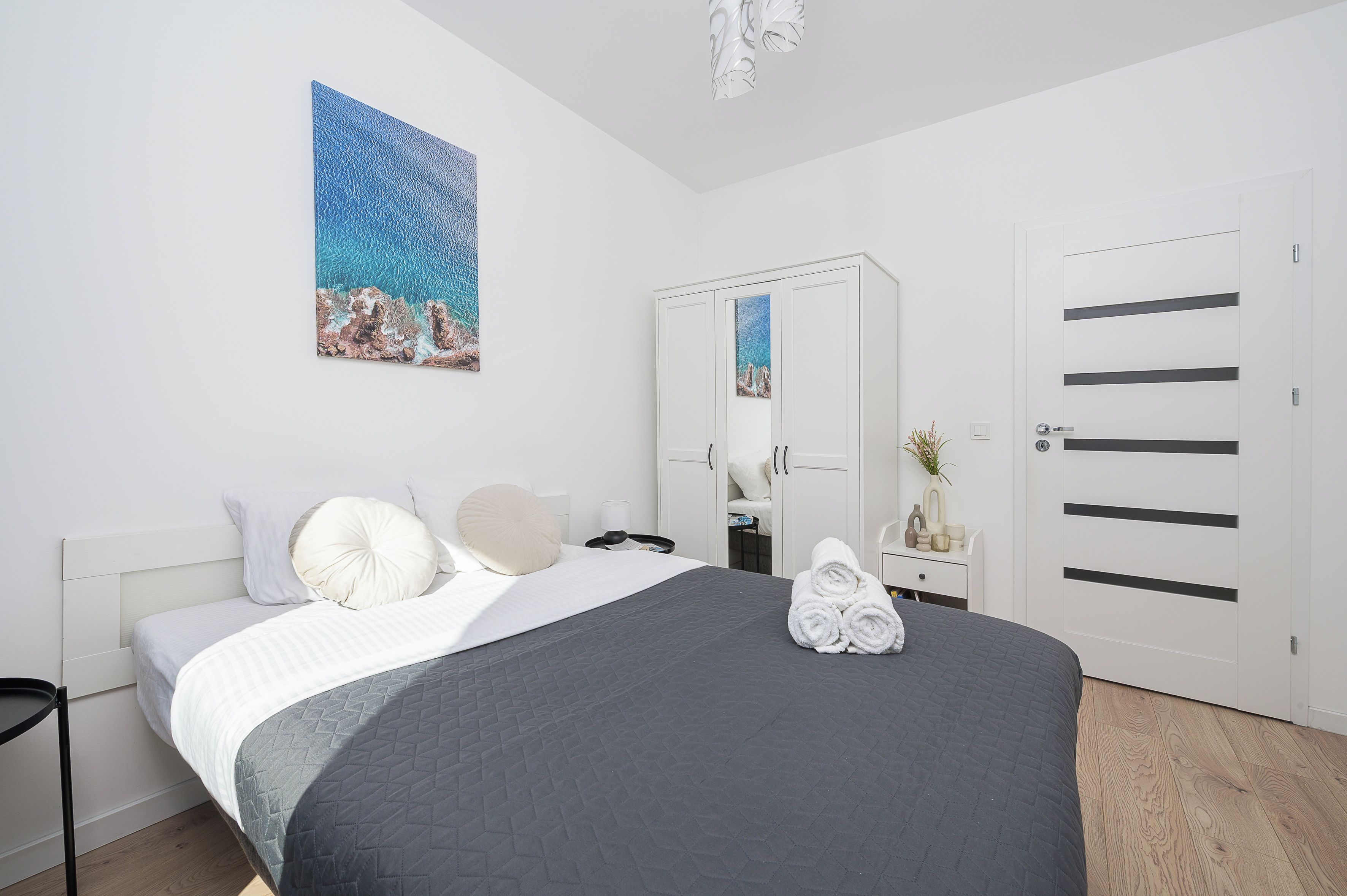 A bedroom with a bed, pillows, a bedside table with a lamp, a mirror, and a wardrobe.