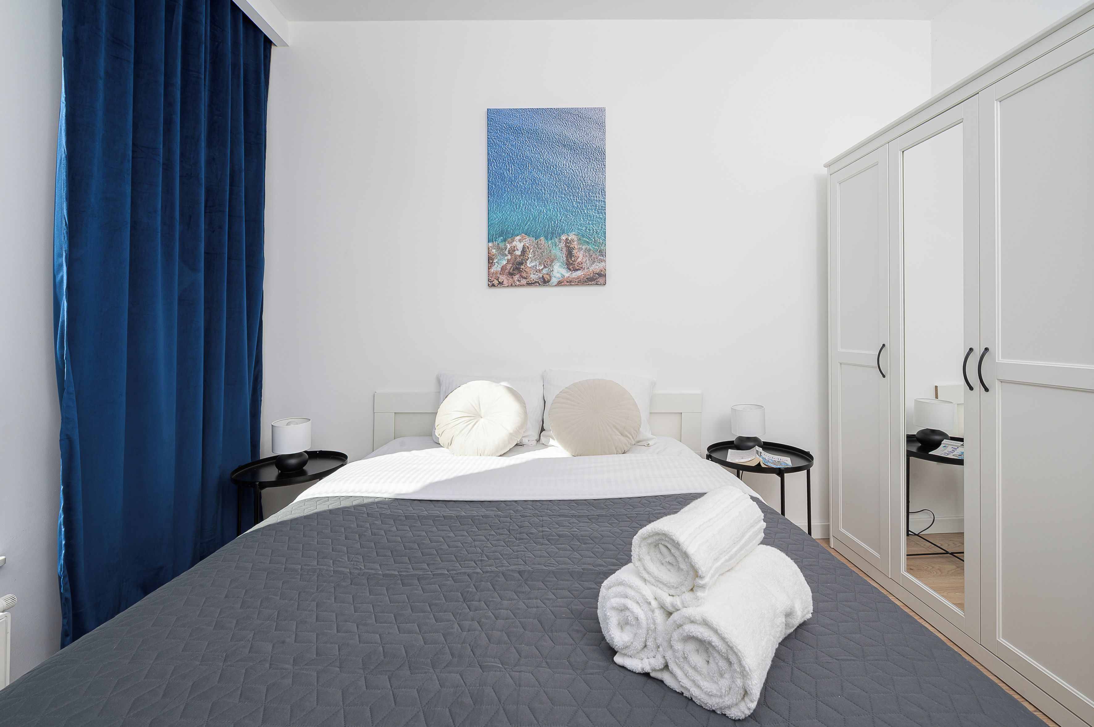 A hotel room with a bed, a nightstand, a desk, a wardrobe, and a painting on the wall.
