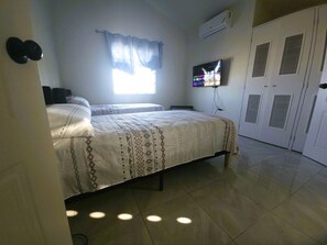 A bedroom with a bed, a television, a wardrobe, and a window with curtains. - Camelot Blue - A Tranquil Oceanview Escape (Discovery Bay)