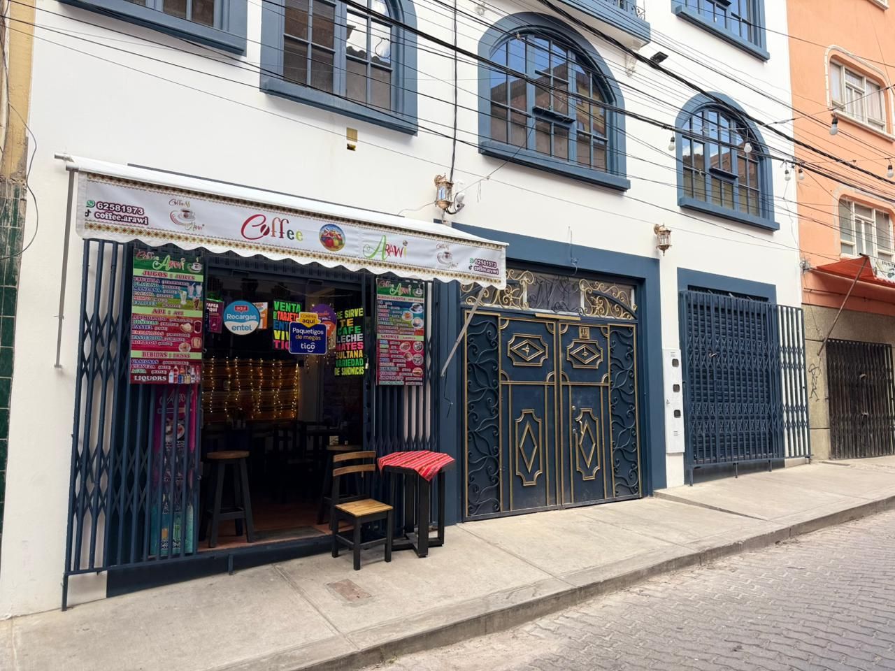 A storefront with a signboard, a metal gate, and a small stool outside.
