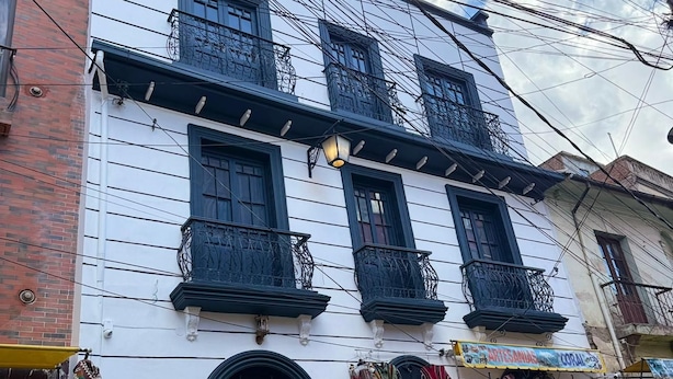 A multi-story building with balconies, a ground-level shop with various items on display, and a clear sky. - Casona Tambo La Paz Hotel Boutique (La Paz)