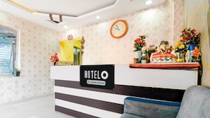 Zona de recepción de un hotel con mostrador, un reloj y una estatua de una deidad.
