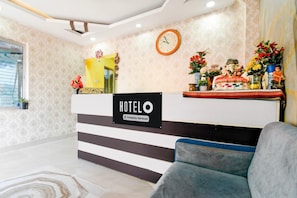 Un hall d'hôtel comprenant un comptoir d'accueil, une horloge et une statue représentant une divinité.