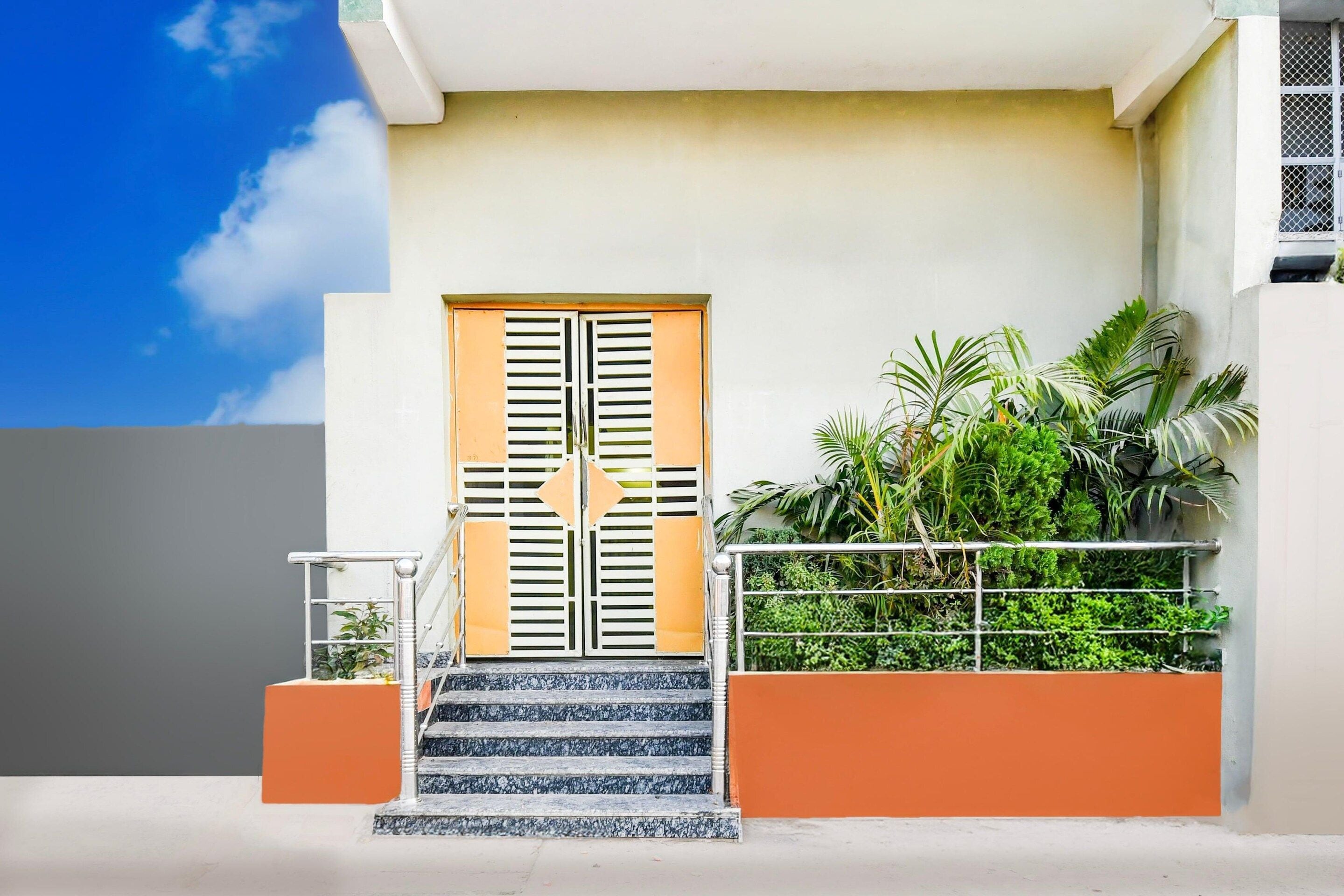 Un edificio moderno con un'entrata doppia, una scala e un piccolo giardino con piante.