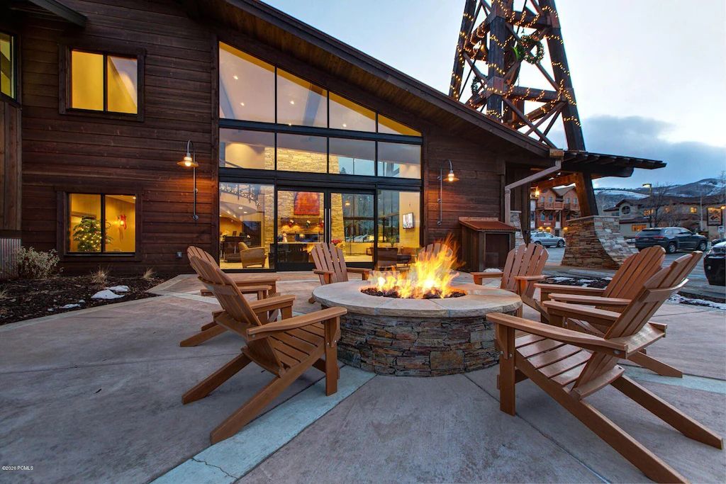 A wooden building with large windows and a fire pit with chairs.