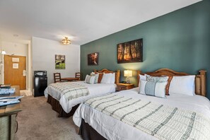 A hotel room with two beds, a desk, a chair, a refrigerator, and artwork on the walls. - TWO Queen Beds, No Stairs, Winter Hot Tub | Moose Mgmt 817 (Park City)