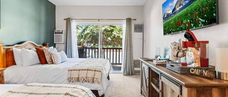 Habitación de hotel con dos camas, un escritorio de madera, un cuadro y vista a un jardín a través de un ventanal.