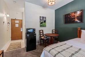 Ein Hotelzimmer mit einem Bett, einem kleinen Tisch mit Stühlen, einer Mikrowelle, einem Kühlschrank, einer Tür mit einem Hinweis, einem Bild und einer Wandleuchte.
