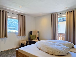 Ein Schlafzimmer mit Bett, Stuhl, einem Fenster mit Vorhängen und Blick ins Freie.
