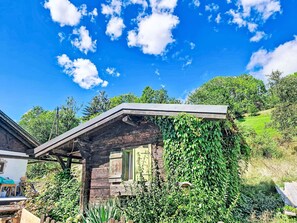 Eine rustikale Holzhütte mit geneigtem Dach, umgeben von üppiger Vegetation und Bäumen.