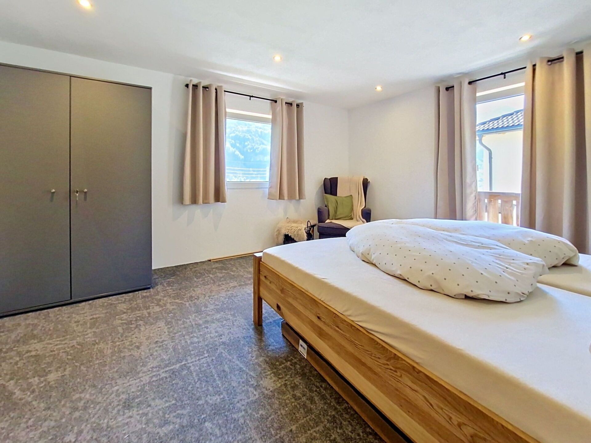 A bedroom with a bed, a wardrobe, a window with curtains, and a view of the outside.