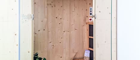 A wooden sauna room with a bench, a plant, and a box of floor cleaner.