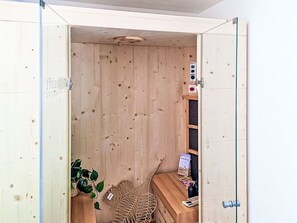 Un sauna de madera con un banco, una planta y una caja de limpiador para el suelo.