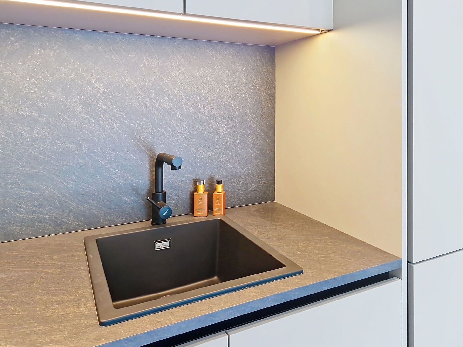 A modern bathroom with a black sink, a single faucet, and two bottles of shampoo.