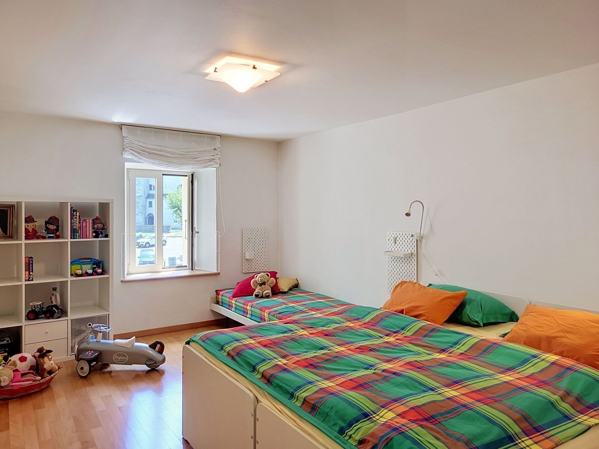 Ein Kinderzimmer mit zwei Betten, einem Bücherregal und einem Fenster.
