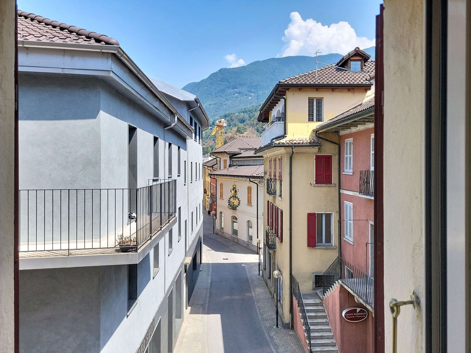A narrow street with buildings on either side, a clear sky, and a mountain in the background.