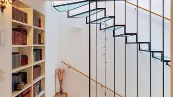 Eine Treppe mit einem geometrischen Geländer, ein Bücherregal voller Bücher und eine dekorative Vase auf dem Boden.