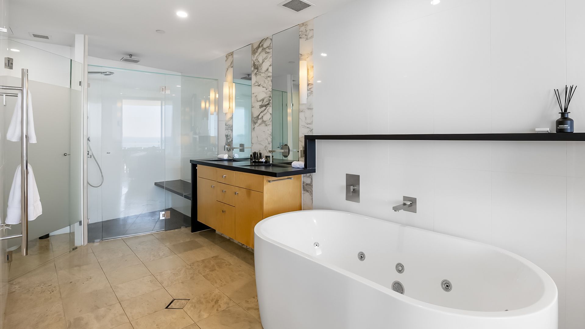 Une salle de bain moderne dotée d’une douche à parois de verre, d’une baignoire sur pieds et d’un meuble-lavabo avec un pare-feu en marbre.
