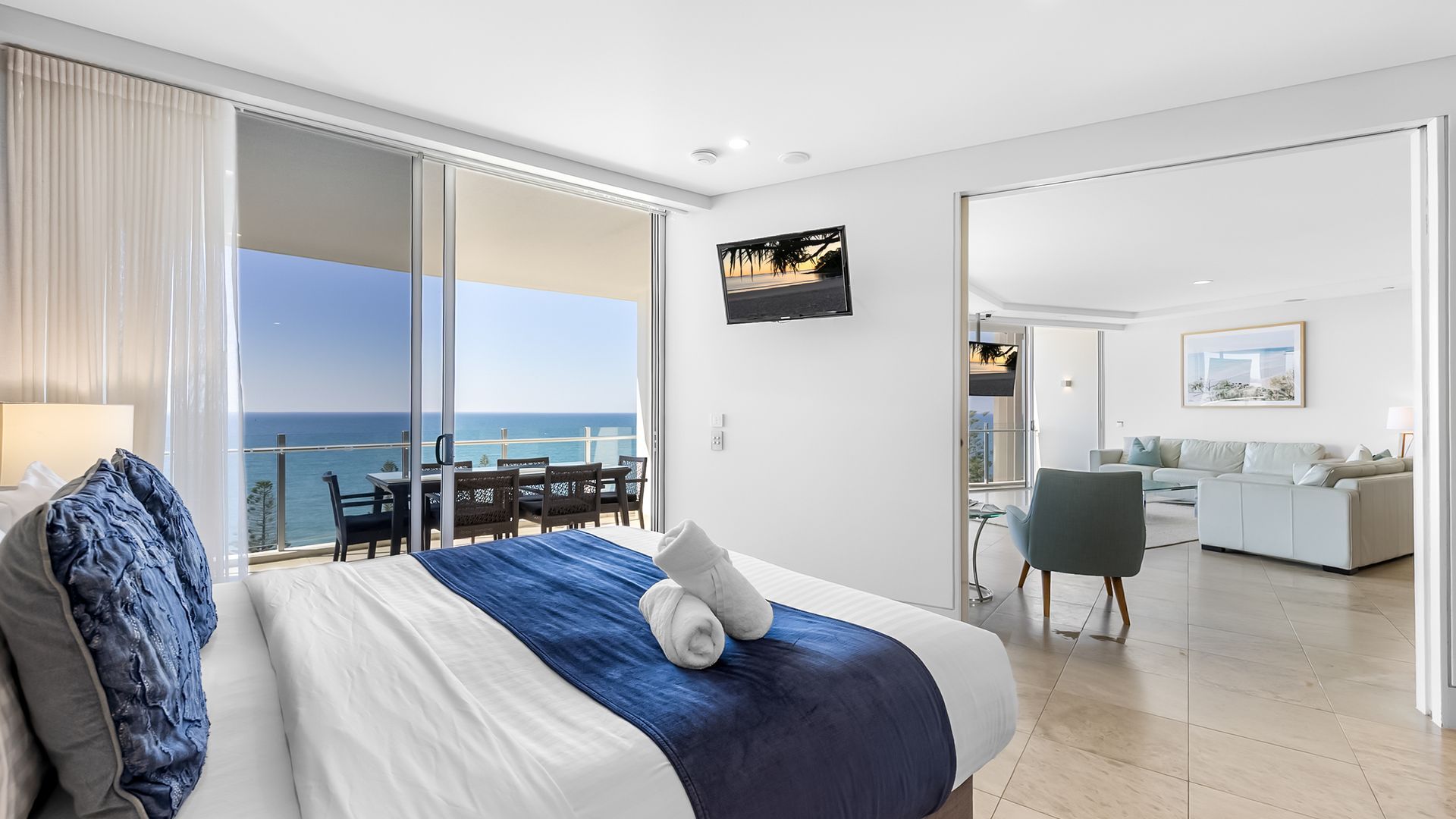 A hotel room with a bed, a balcony with a view of the sea, a dining area, and a living space.
