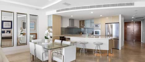 A modern kitchen with a central island, stainless steel appliances, and a dining area with a glass table and white chairs.