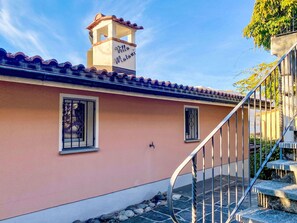 Ein Gebäude mit rosa Fassade, einem Ziegeldach, einem kleinen Turm mit Balkon und einer Wendeltreppe.