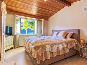 A bedroom with a bed, a television, a dresser, and a window with a view of palm trees. - Beautiful private villa for 6 guests with A/C, WIFI, TV and patio (Ranzo)