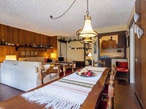 Ein gemütliches Wohnzimmer mit einer Couch, einem Esstisch mit Platzdeckchen und einer Küchenzeile mit Holzschränken und einem roten Gerät.