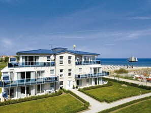 A multi-story hotel with balconies overlooking a beach, a clear sky, and a sailboat in the distance. - 4 ,,ut de Franzosentid (Kuehlungsborn)