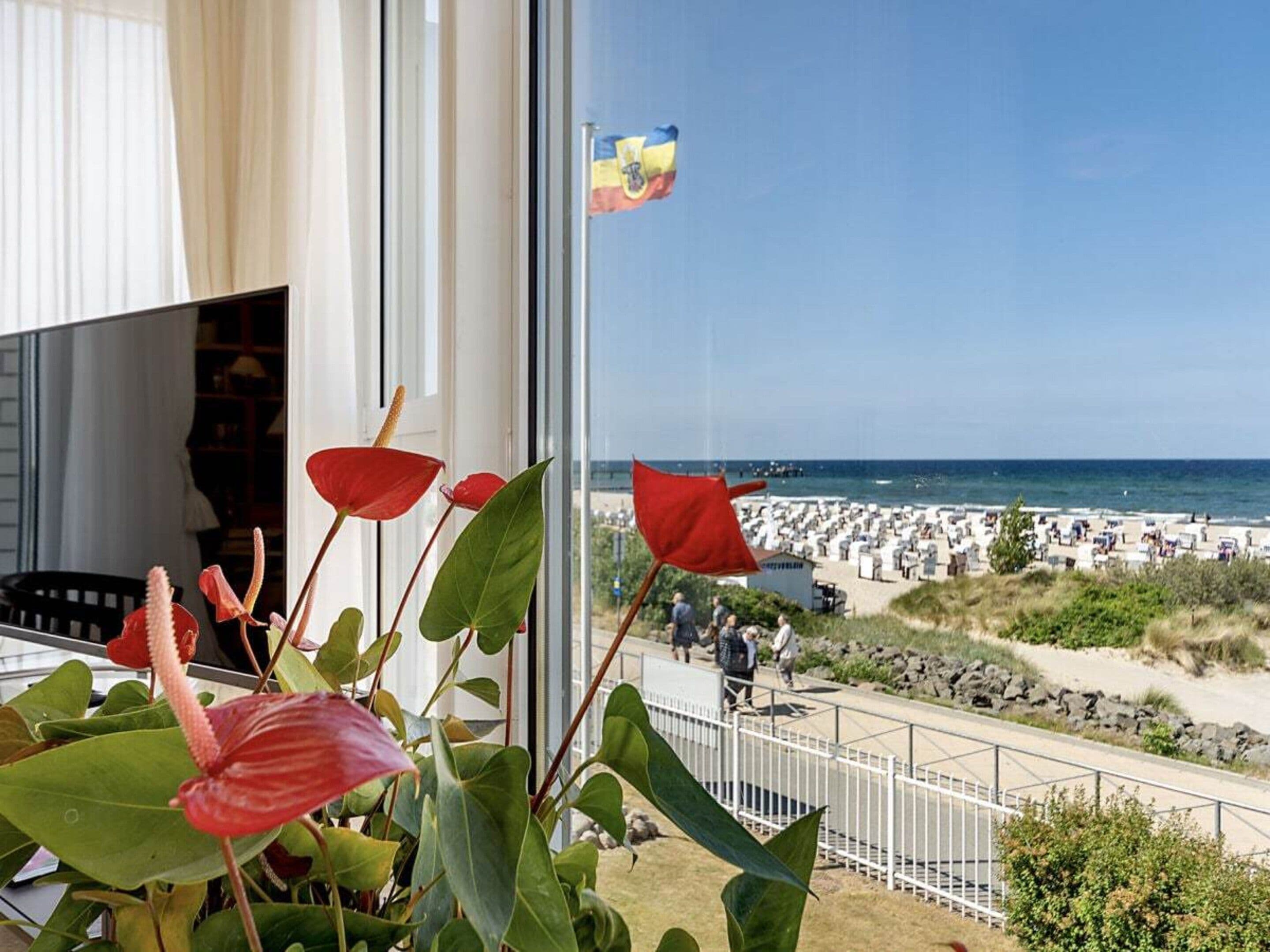 Ein Balkon mit roten Blumen, Blick auf den Strand und eine Flagge.