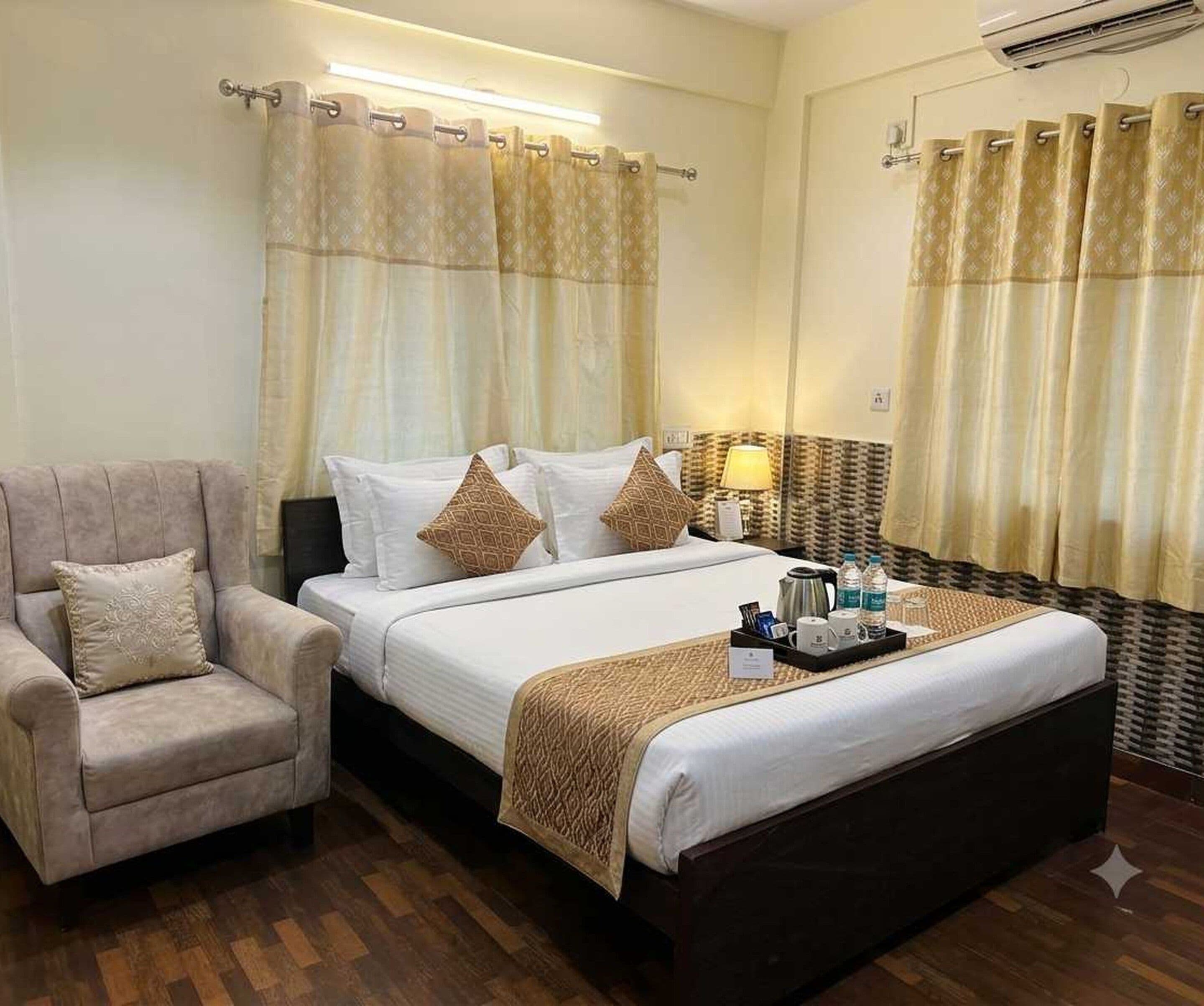 A hotel room with a bed, a chair, a bedside table with a lamp, and curtains.