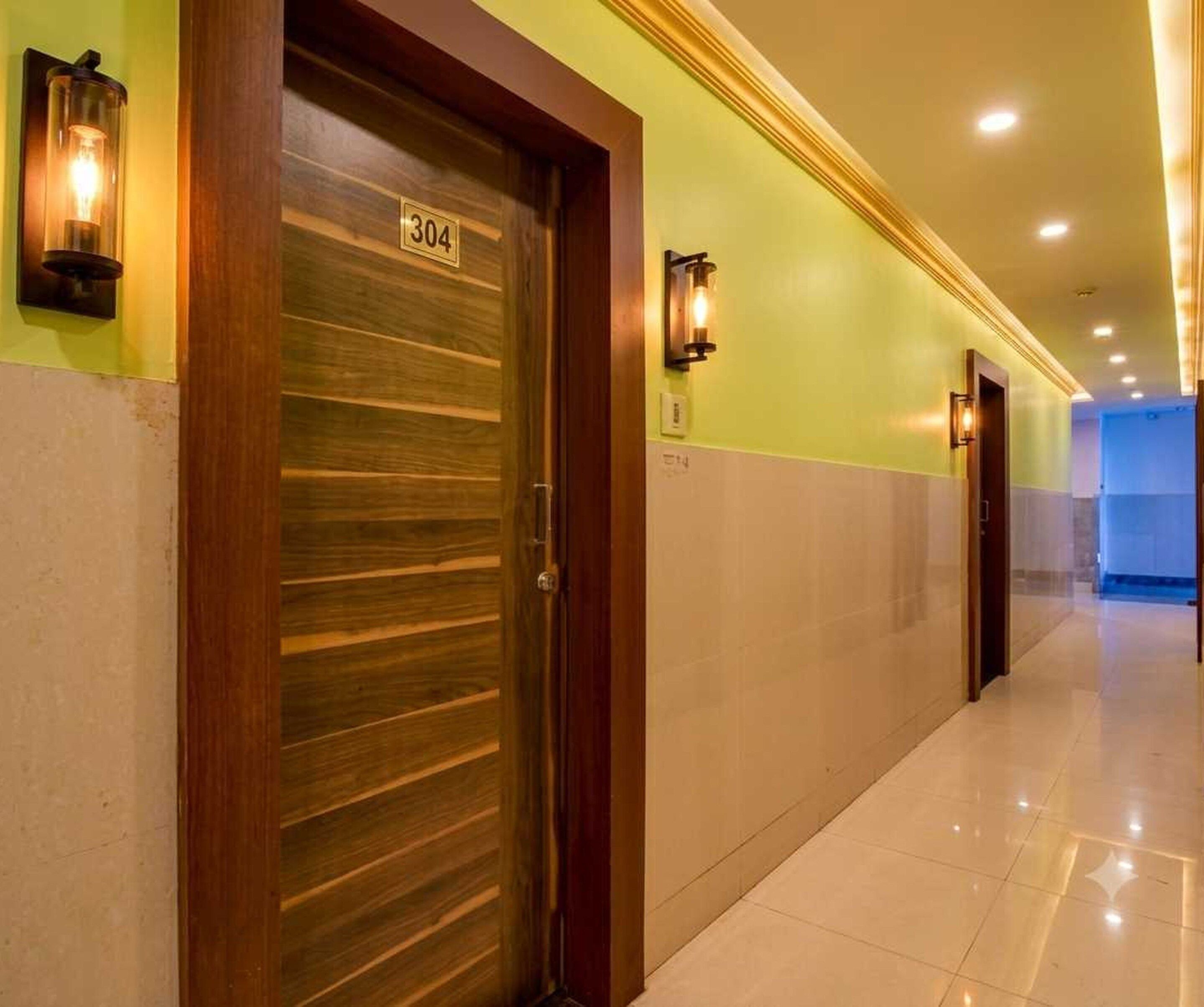 Een hotelgangen met een houten deur met daarop '304', een lamp en een betegelde vloer.