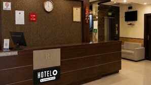 Un mostrador de recepción de hotel con un reloj, un cartel de 'No Fumar' y un cartel con los horarios de registro.