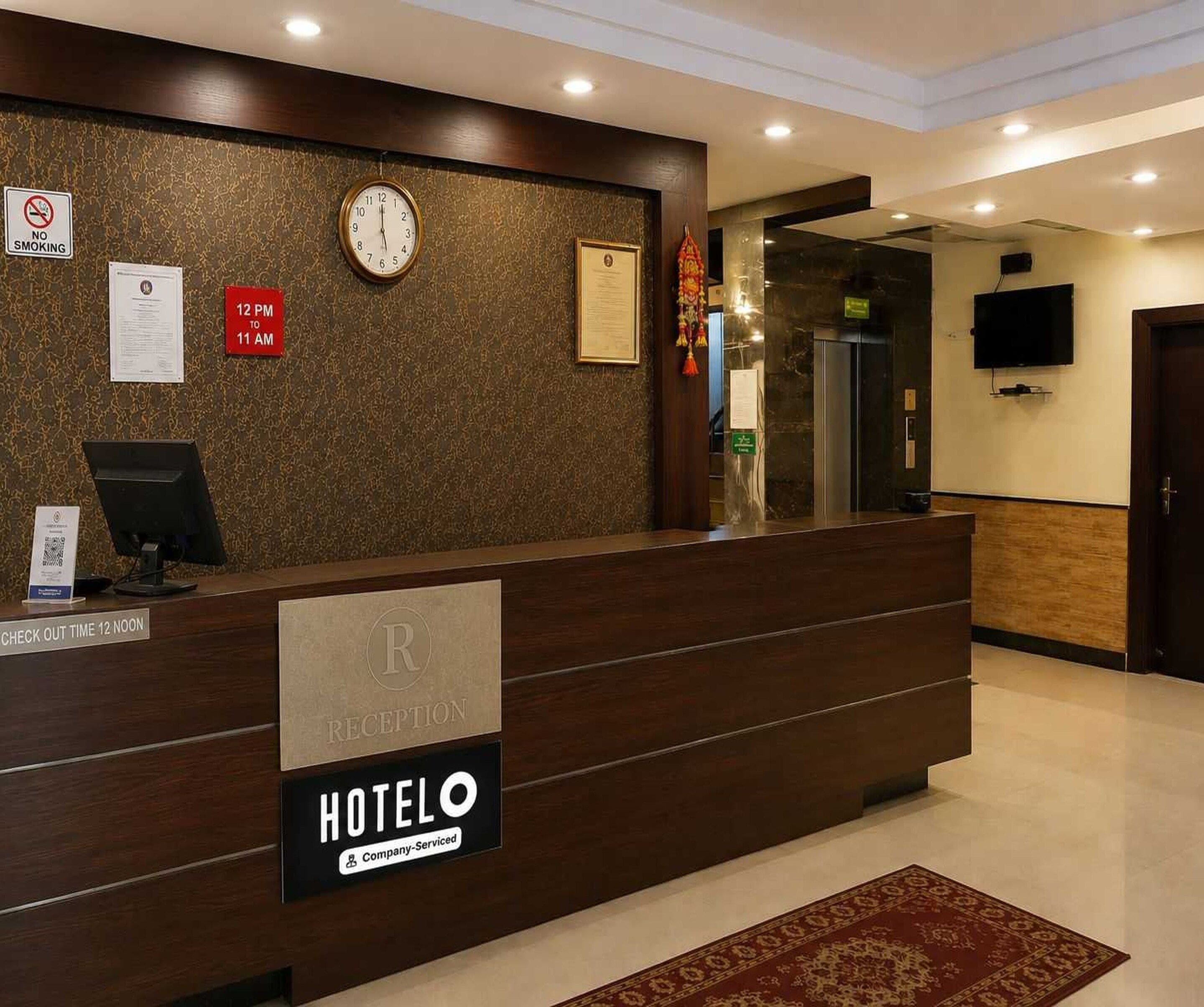 A hotel reception desk with a clock, a no-smoking sign, and a check-out time sign.